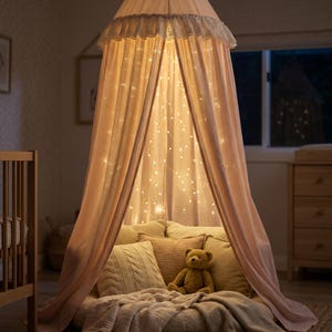 K&ouml;nnte beinhalten: Ein hellrosa Stoffhimmel h&auml;ngt von der Decke, mit einem ger&uuml;schten oberen Rand und innenliegenden Lichterketten. Im Inneren befindet sich ein rundes Bodenkissen, das mit mehreren strukturierten Kissen und einer weichen Decke sowie einem kleinen Teddyb&auml;ren ausgelegt ist.