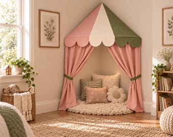 Può includere: Una tenda da gioco angolare con un baldacchino smerlato nei colori rosa, crema e verde salvia. La tenda presenta tende rosa abbinate legate con fasce di tessuto verde. All'interno, un tappeto rotondo color crema con vari cuscini decorativi.