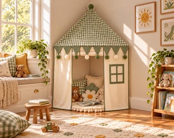 Può includere: Una tenda da gioco angolare con tetto a quadretti vichy verdi e bianchi, pareti in tessuto color crema, una finestra quadrata e un bordo decorativo di bandierine triangolari verdi con piccoli pon pon. L'interno contiene cuscini e giocattoli.