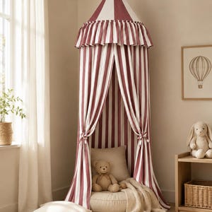 May include: A floor-to-ceiling fabric canopy featuring vertical stripes in dark red and white. The canopy has a conical top with a ruffled valance and two side panels tied back to reveal a beige floor cushion, a teddy bear, and a throw blanket.