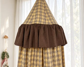 Può includere: Un baldacchino in tessuto di forma conica con un motivo a quadri giallo e marrone. La sezione superiore è un cono appuntito, mentre la parte inferiore è composta da lunghi pannelli di tessuto drappeggiato. Un'ampia balza marrone scuro circonda il centro.