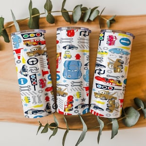 May include: Three white insulated tumblers with colorful car-themed designs. Each tumbler features illustrations of various cars, tools, and traffic signals. The tumblers have a silver rim and a clear lid, perfect for hot or cold beverages.