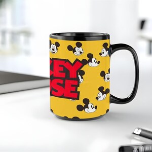 Peut inclure: Un mug en c&eacute;ramique jaune avec une anse et un bord noirs, orn&eacute; d'un motif r&eacute;p&eacute;titif de visages de Mickey Mouse et du texte rouge en gras MICKEY MOUSE sur le c&ocirc;t&eacute;. Le mug pr&eacute;sente une forme cylindrique et une finition brillante.