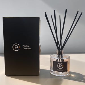 May include: A clear glass diffuser bottle with black reeds and a black box. The bottle has a label with the brand name "Pookie Candles" and the scent "Bergamot, Rosemary & Peppermint". The black box also has the brand name and logo.