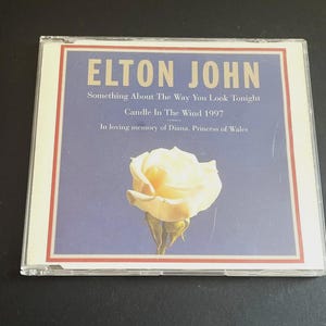 Può includere: Custodia di un CD dell'album di Elton John, "Something About The Way You Look Tonight". La copertina presenta una rosa color crema su sfondo blu, con il testo "Candle In The Wind 1997" e "In loving memory of Diana, Princess of Wales."