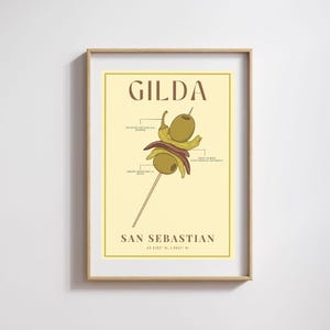 Op de afbeelding: Een ingelijste print met een Gilda-spiesillustratie. Het kunstwerk bevat olijven, pepers en ansjovis, met tekst die de ingrediënten en de stad San Sebastian labelt.