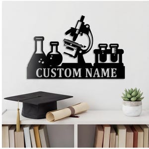 Puede incluir: Un letrero de pared de metal negro con la silueta de un microscopio, dos matraces de laboratorio y un soporte para tubos de ensayo. Debajo del equipo científico, una barra rectangular muestra el texto CUSTOM NAME en letras blancas.