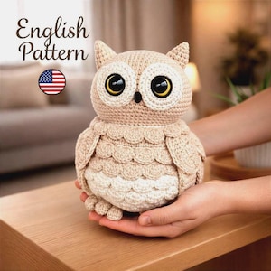 Könnte beinhalten: Eine beige und cremefarbene gehäkelte Eule mit großen gelben und schwarzen Augen, einem kleinen schwarzen Schnabel und texturierten federartigen Maschen. Der Text English Pattern ist oben links neben einem kleinen US-Flaggen-Symbol zu sehen.