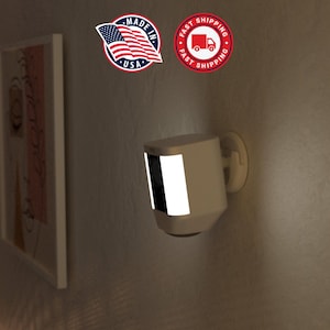 May include: A beige security camera with a bright white light strip is mounted on a wall. The camera has a dark lens and is attached to a white mounting bracket. The image also includes a "Made in USA" sticker and a "Fast Shipping" sticker.