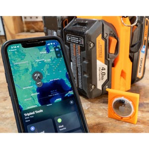 May include: A smartphone displaying a map with the text "Tripled Tools" and a wrench icon. An orange AirTag holder and a black and orange power tool battery are in the background.