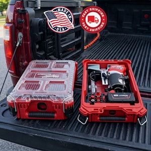 May include: A red Milwaukee Packout storage case with a clear lid and a matching red open case containing a cordless power tool, a battery, and various metal drill bits, all resting on the black ribbed bed of a pickup truck.
