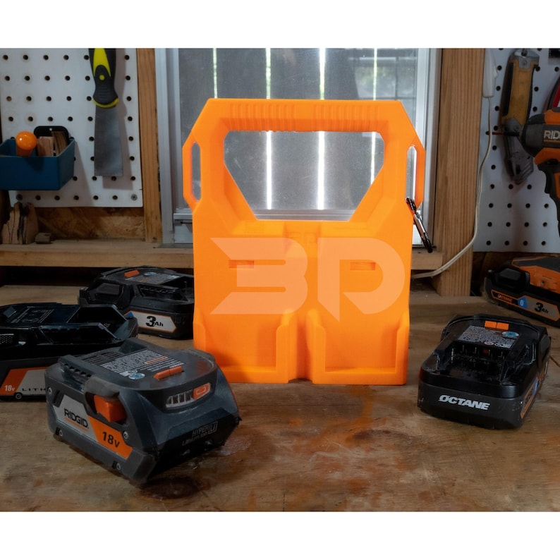 May include: An orange 3D-printed battery holder with a handle and the letters "3D" printed on the front. Several black and gray 18V and 3Ah batteries are arranged around the holder on a wooden surface. A carabiner is attached to the holder.