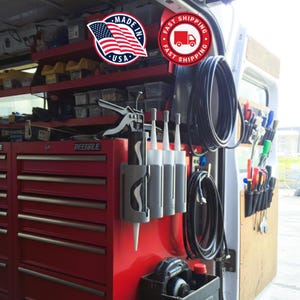 May include: A red toolbox and storage system inside a van, with various tools, supplies, and equipment. Includes a "Made in USA" sticker and a "Fast Shipping" sticker. The image shows a well-organized workspace.