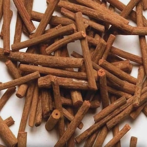 Könnte beinhalten: Nahaufnahme eines Haufens brauner, zylindrischer Stäbe. Die Stäbe variieren in Länge und Dicke und weisen eine raue, strukturierte Oberfläche auf. Die Enden einiger Stäbe zeigen ein helleres, rotbraunes Inneres. Die Stäbe liegen auf weißem Grund.