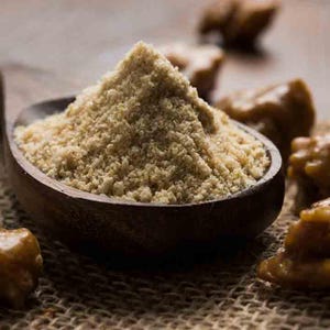 May include: A wooden spoon holds a pile of light brown powder, with several amber-coloured, irregularly shaped pieces scattered around it. The spoon rests on a hessian surface. The image is a close-up shot.