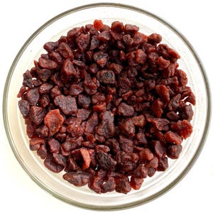 May include: A clear glass bowl filled with dried, dark red fruit pieces. The fruit pieces have a wrinkled texture and vary in size. The bowl is set against a white background, highlighting the color and texture of the fruit.