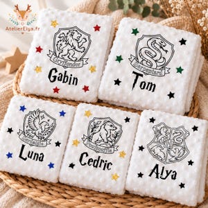 Peut inclure: Cinq couvertures blanches en tissu minky à relief, ornées d'écussons et de prénoms imprimés en noir. Les motifs incluent Gryffondor avec Gabin, Serpentard avec Tom, Serdaigle avec Luna, Poufsouffle avec Cedric et un écusson combiné avec Alya.