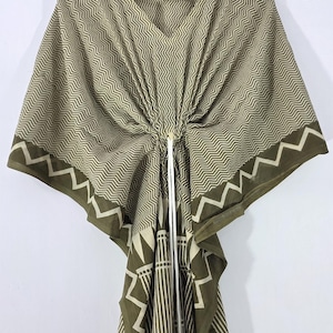 May include: Olive green kaftan with a geometric zigzag pattern and white drawstring. The kaftan features a V-neck and a contrasting border with a white zigzag design. The fabric is lightweight and appears to be cotton.