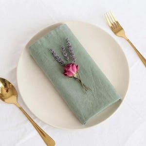 Saliegroene servetten en minimalistische tafelsetting op een strak wit oppervlak.