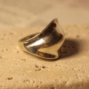 May include: A silver ring with a smooth, curved design. The ring has a polished finish, reflecting light. The ring is set against a neutral background, highlighting its shape and metallic sheen. A piece of jewellery.