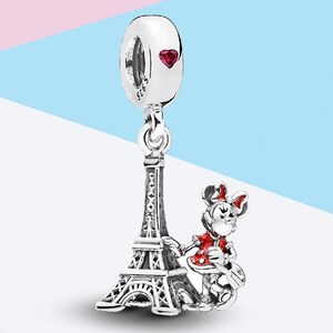 May include: A silver charm featuring a red heart-shaped gem and a Minnie Mouse figure in a red dress, standing next to a detailed Eiffel Tower. The charm is made of 925 silver.