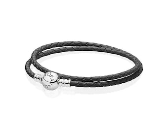 May include: A black double-wrap leather bracelet with a silver clasp. The bracelet features a braided leather design and a round clasp with the brand name engraved on it. The bracelet is displayed on a white background.