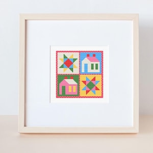Peut inclure: Une œuvre d'art encadrée en point de croix avec quatre carrés colorés. Chaque carré présente un motif différent : un éclat d'étoile, une maison et une combinaison des deux. L'œuvre est encadrée dans un cadre en bois clair.