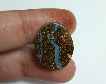 May include: Oval-shaped gemstone with a dark brown base, speckled with gold and featuring striking blue veins. The polished surface of the stone reflects light, highlighting the intricate patterns. This gemstone is a unique piece for jewelry or collection.
