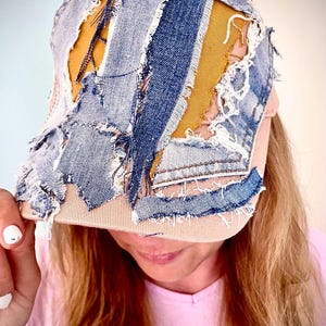 Könnte beinhalten: Eine Baseballkappe mit einem Patchwork-Design aus ausgefransten blauen Denim-Streifen und senfgelben Stoffbahnen. Die Kappe hat einen hellbraunen Schirm und eine Grundkappe mit sichtbaren ausgefransten Kanten und durchgehenden, unebenen Nähten.