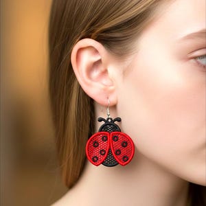 Könnte beinhalten: Bestickte Marienkäfer-Ohrringe in Rot und Schwarz. Die Ohrringe haben einen schwarzen Kopf und Fühler, mit roten Flügeln, die mit schwarzen Punkten verziert sind. Sie hängen an silberfarbenen Haken.