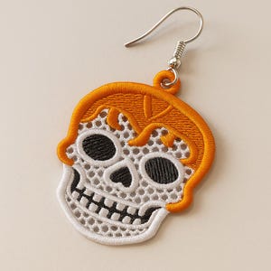 May include: Embroidered skull earring with orange hair and a white skull design. The skull has black eye sockets and teeth. The earring has a silver hook.