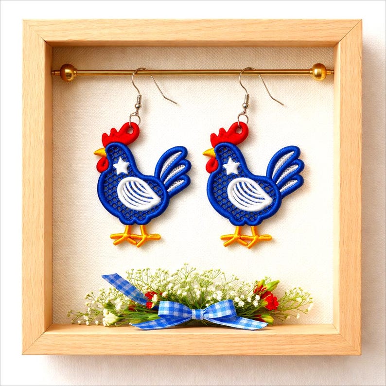 May include: A pair of rooster-shaped earrings with blue, white, red, and yellow accents. The earrings are displayed in a wooden frame with a decorative bow and floral arrangement. The rooster design features a star on the chest.