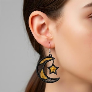 Può includere: Un orecchino a forma di luna crescente e stella nero e oro. La luna ha un contorno nero con un interno ricamato in oro e un design a rete. Una stella dorata pende dalla luna. L'orecchino è sospeso a un gancio d'argento.