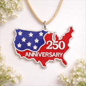 May include: A patriotic pendant in the shape of the United States, featuring a red and blue design with white stars and the number "250" in white. The word "ANNIVERSARY" is also displayed. The pendant hangs from a beige rope.