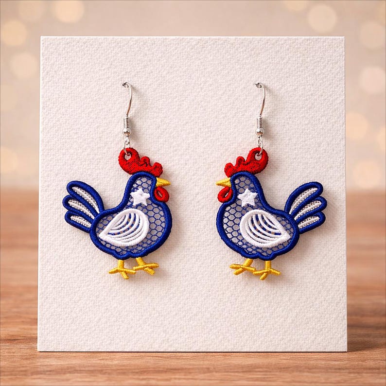 May include: A pair of rooster-shaped earrings. The earrings feature a blue body with white and red accents, a white star, and yellow feet. The earrings are displayed on a white card.