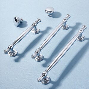 May include: A collection of polished chrome cabinet hardware, including knobs and bar pulls. The hardware features a reflective surface and decorative detailing, suitable for kitchen or bathroom cabinetry. The pulls vary in length, offering design flexibility.