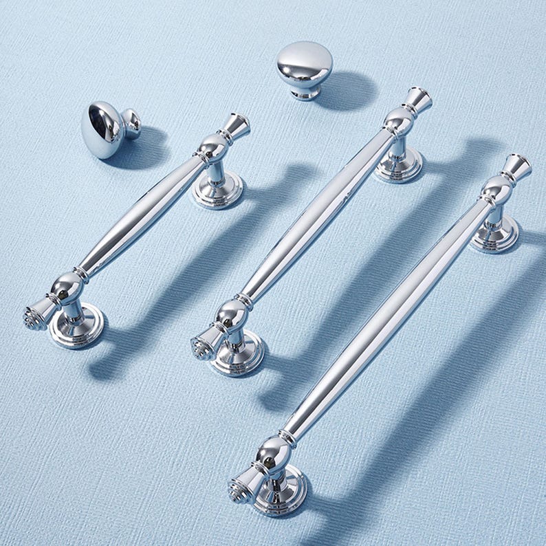 May include: A collection of polished chrome cabinet hardware, including knobs and bar pulls. The hardware features a reflective surface and decorative detailing, suitable for kitchen or bathroom cabinetry. The pulls vary in length, offering design flexibility.