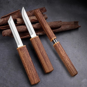 Puede incluir: Tres cuchillos con mangos de madera y hojas plateadas. Los mangos tienen un patrón de vetas de madera y son de color marrón medio. Las hojas son rectangulares y tienen un borde afilado. Los cuchillos se exhiben sobre una superficie gris oscuro con palitos de canela en el fondo.