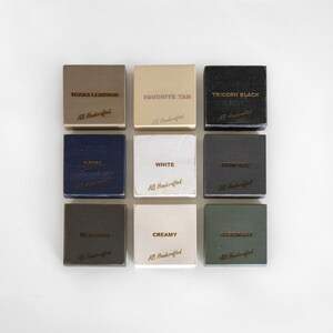 Puede incluir: Nueve muestras cuadradas de cuero en varios colores, incluyendo "Texas Leather", "Favorite Tan" y "Tricorn Black". Cada muestra tiene texto y las palabras "AB Handcrafted" en una fuente cursiva. Las muestras est&aacute;n dispuestas en una cuadr&iacute;cula de 3x3.