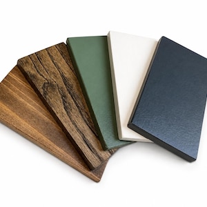 May include: A set of five rectangular wooden boards arranged in a fan shape. The boards feature distinct finishes including two natural wood grain textures in light and dark brown, followed by solid matte colors in sage green, white, and charcoal black.