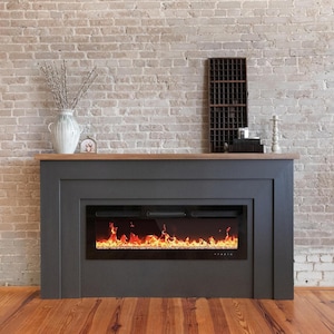 May include: A dark gray electric fireplace with a realistic flame effect, set against a light brick wall. The fireplace has a wooden mantel and is decorated with a vase, decorative items, and a wine rack.