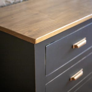 Puede incluir: Una c&oacute;moda gris oscuro con una tapa de madera marr&oacute;n claro. Tiene seis cajones con tiradores dorados. La tapa de madera tiene un patr&oacute;n de vetas natural. La c&oacute;moda es de estilo moderno.