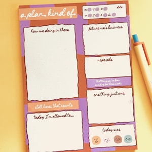May include: A colorful notepad with a whimsical design. The notepad features sections with phrases like "a plan, kind of," "future me's business," and "today I'm allowed to..." A pen with an orange clip rests on the side.