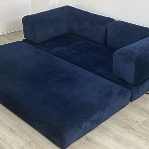 May include: A navy blue modular sofa with a corduroy-like texture, featuring a low-profile design, thick rectangular cushions, and a sleek silver-toned metal frame support on the side. The sofa includes an extended chaise section.