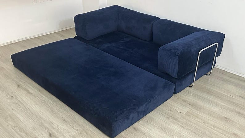 May include: A navy blue modular sofa with a corduroy-like texture, featuring a low-profile design, thick rectangular cushions, and a sleek silver-toned metal frame support on the side. The sofa includes an extended chaise section.