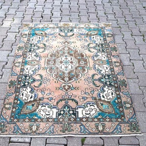 Può includere: Un tappeto rettangolare in stile vintage con un motivo a medaglione centrale. Il tappeto presenta una tavolozza di colori pesca, verde acqua, marrone e bianco. Intricati motivi floreali e geometrici adornano la superficie del tappeto, creando un aspetto dettagliato e ornato.