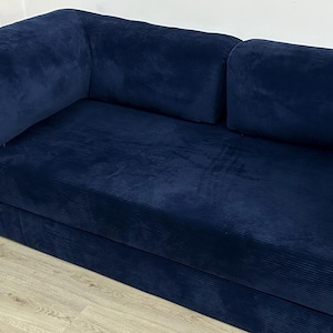 May include: A deep navy blue sofa upholstered in a textured corduroy fabric. The piece features a low-profile design with a long, continuous seat cushion and two large, rectangular armrests positioned at each end of the frame.