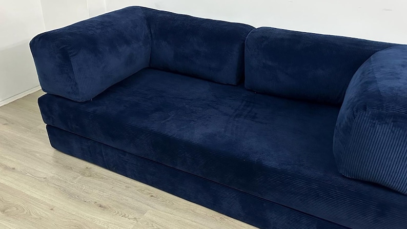 May include: A deep navy blue sofa upholstered in a textured corduroy fabric. The piece features a low-profile design with a long, continuous seat cushion and two large, rectangular armrests positioned at each end of the frame.
