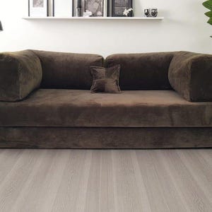 May include: A dark brown corduroy sofa featuring a low-profile design with thick, rectangular armrests and a matching square throw pillow centered on the back cushions. The upholstery has a distinct ribbed texture throughout the entire frame.