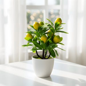 May include: A potted artificial lemon tree with bright yellow lemons and green leaves. The plant is in a white ceramic pot, sitting on a white table. The background includes a window with sheer white curtains.